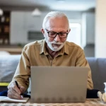 Homme souriant devant son ordinateur finalisant sa demande de retraite en ligne.