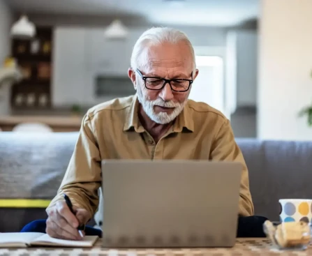 Homme souriant devant son ordinateur finalisant sa demande de retraite en ligne.