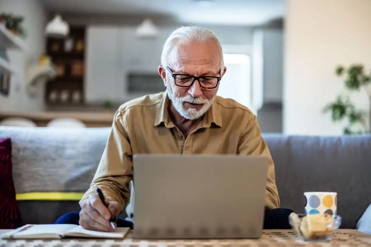 Homme souriant devant son ordinateur finalisant sa demande de retraite en ligne.
