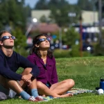 Famille observant ensemble l'éclipse solaire 2026 dans un jardin avec lunettes de protection
