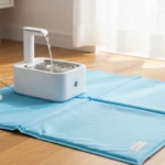 Accessoires pour animaux en été : tapis rafraîchissant bleu et fontaine filtrante pour chat posés dans un intérieur lumineux