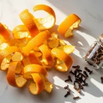 Écorces d'orange séchées et fraîches disposées sur une table en bois avec un bocal et du vinaigre blanc pour recycler les écorces d'orange