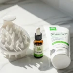 Soins capillaires contre les pellicules : brosse massante en silicone, shampoing spécialisé et huile essentielle de tea tree sur surface blanche